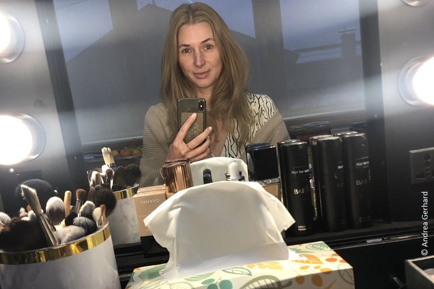 Andrea sitzt vor einem Make-Up Spiegel und macht ein Selfie. 
